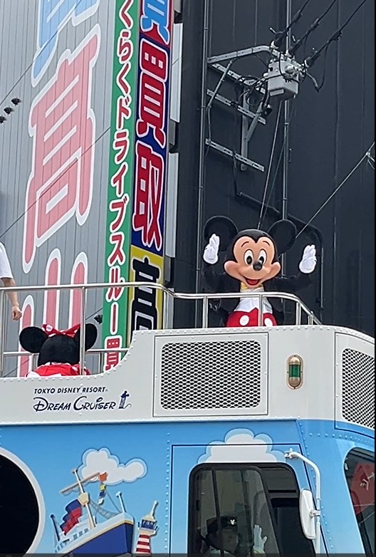 高山質屋の建物を背景に、華やかに装飾されたパレードフロートがゆっくりと進む。フロートの上ではミッキーとミニーが笑顔で手を振り、沿道の観客に夢と喜びを届けている。