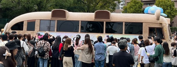 長浦公園に展示されたダッフィーバスの周りに、たくさんの人々が集まり笑顔で写真を撮ったり眺めたりしている様子。ぬいぐるみのような柔らかい質感のバスが公園に佇み、子どもから大人まで多くの来場者がその可愛らしさに魅了されている。